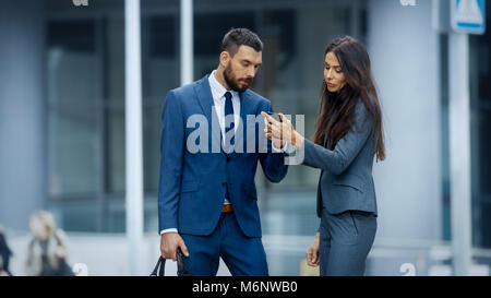 Business Woman and Business Man Use Smartphone and Talk on the Busy Big City Street. Both Look Exquisitely Stylish. Stock Photo