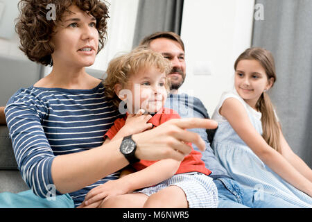 Portrait of happy young family with two children watching TV sitting on sofa in living room and discussing movies Stock Photo