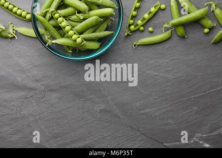 Pods of fresh green peas in glass bowl on stone background, top view Stock Photo