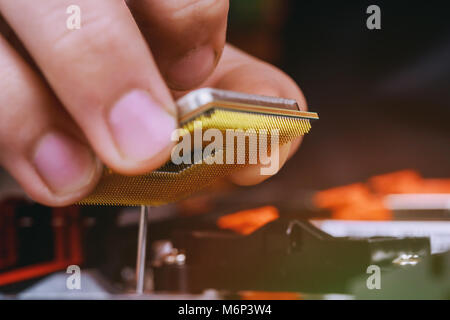 First person view hand holding a computer processor chip on motherboard background. installed in PC motherboard. Stock Photo
