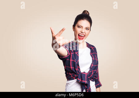 Rock sign. Happy funny toothy smiley young woman showing Rock sign with fingers. studio shot on beige background. focus on face. Stock Photo