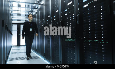 IT Engineer Holding Notebook and Walking Through Data Center Full of Working Rack Servers. Stock Photo