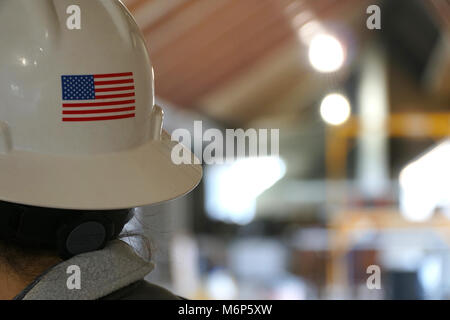Rear portrait photo behind a female construction worker on a building job site. American flag on back of her white hard hat. Woman foreman in charge o Stock Photo