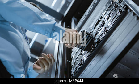 Long Angle Shot In Fully Working Data Center IT Engineer Installs Hard Drive into Server Rack. Detailed and Technically Accurate Footage. Stock Photo