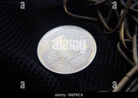 Silver litecoin coin  lying on the  black net surface next to a copper chainl. Cryptocurrency digging difficulty, blockchain and network concept, sele Stock Photo