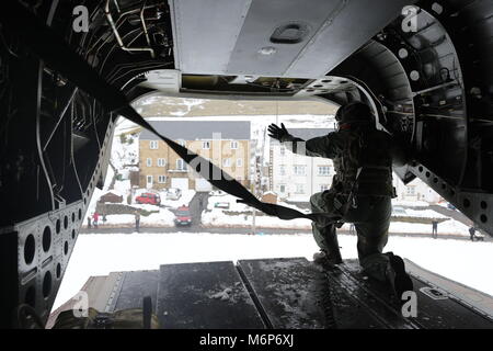A crew members waves to people on the ground from the rear of an RAF Chinook helicopter flying over Cumbria as it delivers supplies to communities in the county which remain cut off after recent heavy snow. Stock Photo