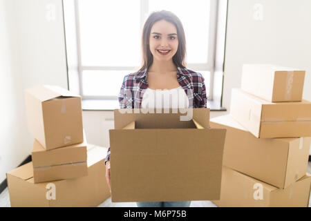Young happy woman carrying a pile of cardboard boxes in her new appartment, she is smiling at camera Stock Photo