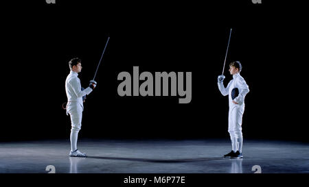 Two Young Professional Fencers Greet Each Other, and Preparing for Fighting Match. Shot Isolated on Black Background. Stock Photo