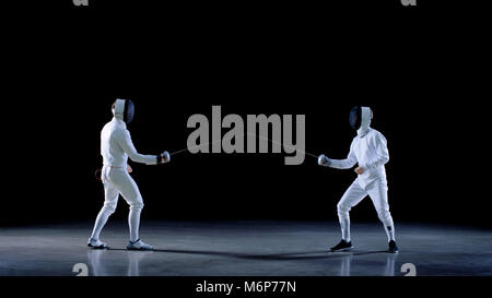 Two Young Professional Fencers Greet Audience, Put on Masks and Start Sword Fighting Match. Shot Isolated on Black Background . Stock Photo