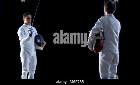 Two Young Fencers Greet Audience and Each Other Before Starting Sword Fighting Match with Foils. Shot on the Isolated Black Background. Stock Photo