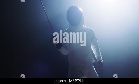 Fully Equipped Fencer Puts Lifts Foil Sword in Readiness for a Match. He Stands in the Spotlight while Darkness is Around Him. Shot Isolated on Black Stock Photo