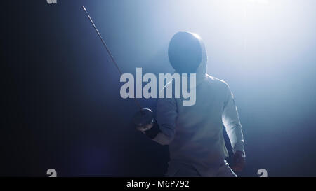 Fully Equipped Fencer Puts Lifts Foil Sword in Readiness for a Match. He Stands in the Spotlight while Darkness is Around Him. Shot Isolated on Black  Stock Photo