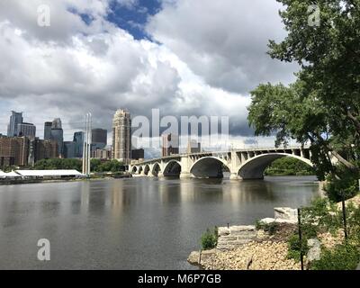 Beautiful establishing shot view of Minneapolis skyline on summer day past the Stone Arch bridge overlooking Mississippi River Stock Photo