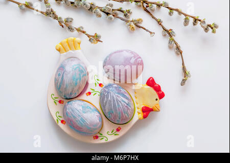 Multicolored Easter eggs lie on a plate in the form of a chicken on a white background with a bouquet of willow branches. The view from the top. The Easter brunch. Stock Photo