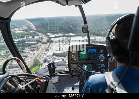 New York City, Circa 2017: Aerial view inside helicopter cockpit flying over suburban area highway traffic on a bright summer day. Over shoulder of pi Stock Photo