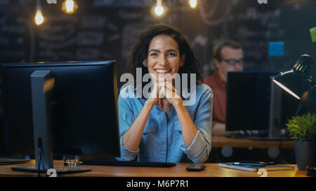 Beautiful Female Office Employee Works at Her Desk on a Personal Computer, She Interrupts Her Work and Smiles Charmingly for the Camera. Stock Photo