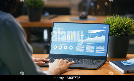 Female Analyst at Her Desk Works on a Laptop Showing Statistics, Graphs and Charts. She Works on the Wooden Table in Creative Office. Stock Photo