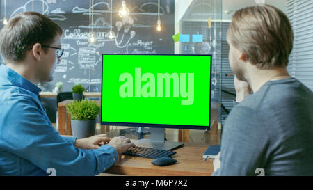 Two Office Employees Have Project Related Discussion, on the Desk Stands Personal Computer with Mock-up Green Screen. They Work in the Creative Office Stock Photo