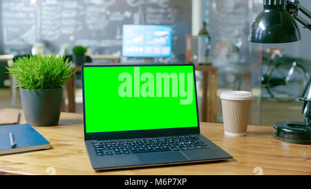Personal Computer with Mock-up Green Screen Monitor Stands on the Office Desk. In the Background Stylish Creative Office at Daytime. Stock Photo