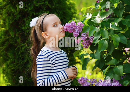 Child smelling lilac flowers. Little girl and lilacs outdoors in the garden. Beautiful spring day. Selective focus. Stock Photo