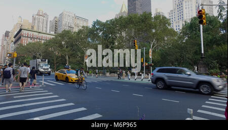 New York City, Circa 2017: Wide view outside NYC park of busy Manhattan intersection of cars passing and people walking across street in safety crossw Stock Photo