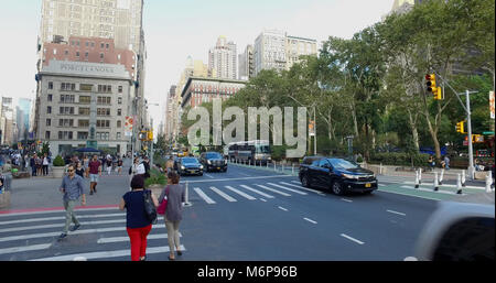 New York City, Circa 2017: Wide view outside NYC park of busy Manhattan intersection of cars passing and people walking across street in safety crossw Stock Photo