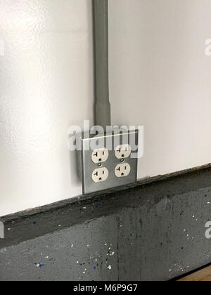 2 gang power outlet receptacle box mounted on a white wall over concrete flooring. Garage workshop type setup. Electrical romex hot neutral and ground Stock Photo