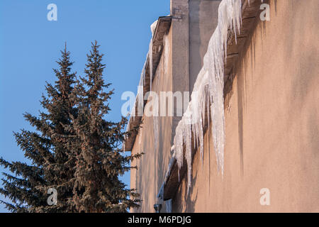 Icicles dangerously hanging from the roof of old house in the winter. Stock Photo