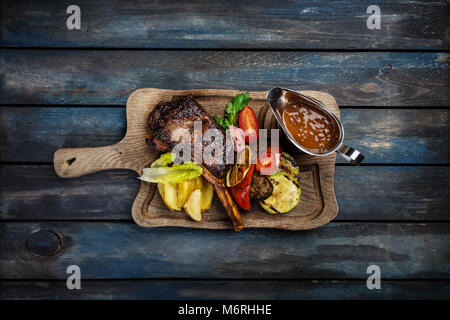 Ribeye steak on bone served with sauce Jack Daniels on the rustic board, with wooden background and top view Stock Photo