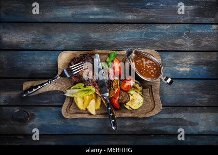 Ribeye steak on bone served with sauce Jack Daniels on the rustic board, with cutlery and wooden background, top view Stock Photo