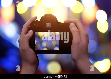 Profesional digital camera in hands. Blue and yellow bokeh in background. Stock Photo