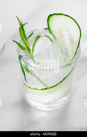 Fresh cocktail with ice, a cucumber slice and tarragon on a white marble table. Macro shot. Stock Photo