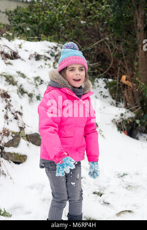 Cute litte girl having fun in the snow. Female child playing in the snowy winter weather wearing a pink coat and blue pompom hat Stock Photo