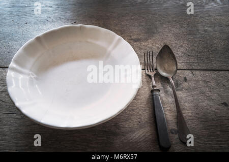 White vintage plate and old rusty metal tableware,  on an aged wooden table. Stock Photo