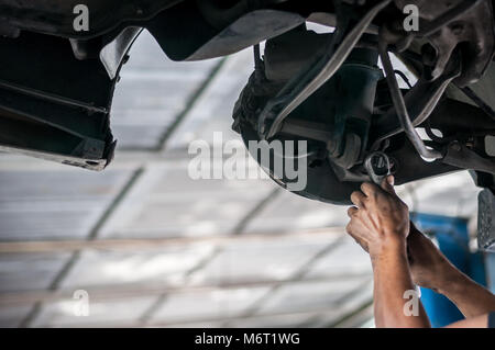 Auto mechanic asian checking bush-bolt under double wishbone suspension by hand with tools car lift Stock Photo