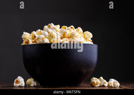 Popcorn in a ceramic bowl on a wooden background.