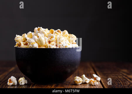 Popcorn in a ceramic bowl and scattered on a wooden background. Stock Photo