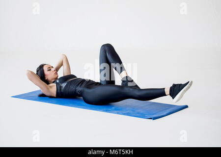 Close-up view of the sports charming woman lying on the mat and doing bicycle crunches in the white studio. Stock Photo