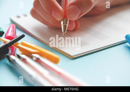 child s hand holds red pen in hand to make note in notepad. Stock Photo