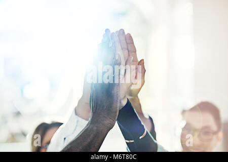 Team of diverse businesspeople standing in a huddle together in a bright modern office high fiving each other Stock Photo