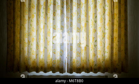Early morning sunlight streaming through a crack in a pair of closed double panel curtains. Stock Photo