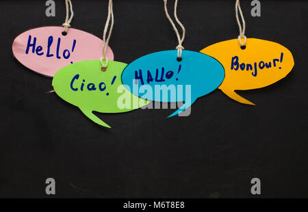Hello / Speaking learning foreign languages. colorful speech bubbles hanging from a cord on blackboard background. Stock Photo