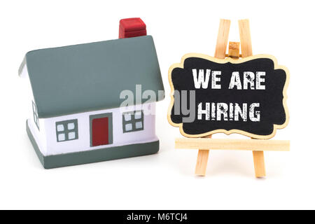 We are Hiring!  inscription on a blackboard and miniature model of house  on a  white background. Stock Photo