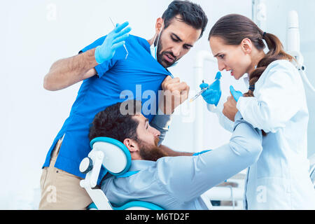 Low-angle view of a funny dentist or dental surgeon acting crazy in front of his female assistant, while having a patient on the chair in the dental o Stock Photo