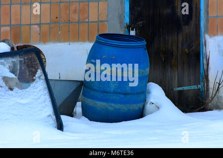 The old blue plastic barrel is thrown into the snow on an abandoned and destroyed factory amidst chaos. Destruction and vandalism. Ukraine. Stock Photo