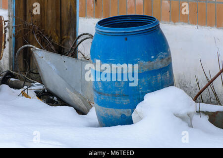 The old blue plastic barrel is thrown into the snow on an abandoned and destroyed factory amidst chaos. Destruction and vandalism. Ukraine. Stock Photo