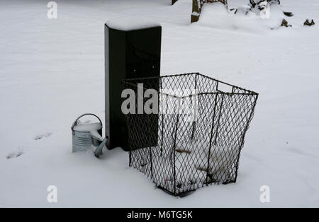 Litter bin, covered tap and watering can in snow, Warwick cemetery, Warwickshire, UK Stock Photo