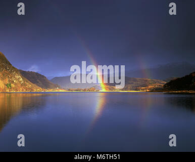 A vivid rainbow brightens up a dark sky over Llyn Dinas in the Snowdonia National Park, Wales. Stock Photo