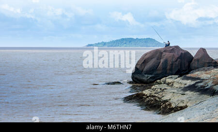 A lonely fisherman sitting on a big rock angling Stock Photo