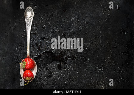 in a spoon a wet strawberry on a dark background with splashes of water, top view. Stock Photo